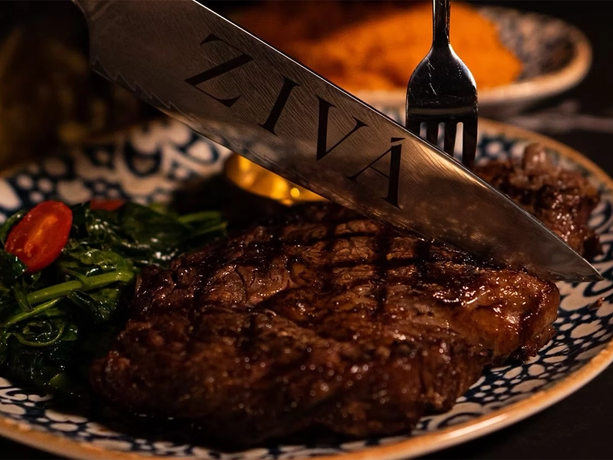 Close-up of a grilled steak served with sautéed vegetables, with a knife engraved ZIVÁ resting on top.